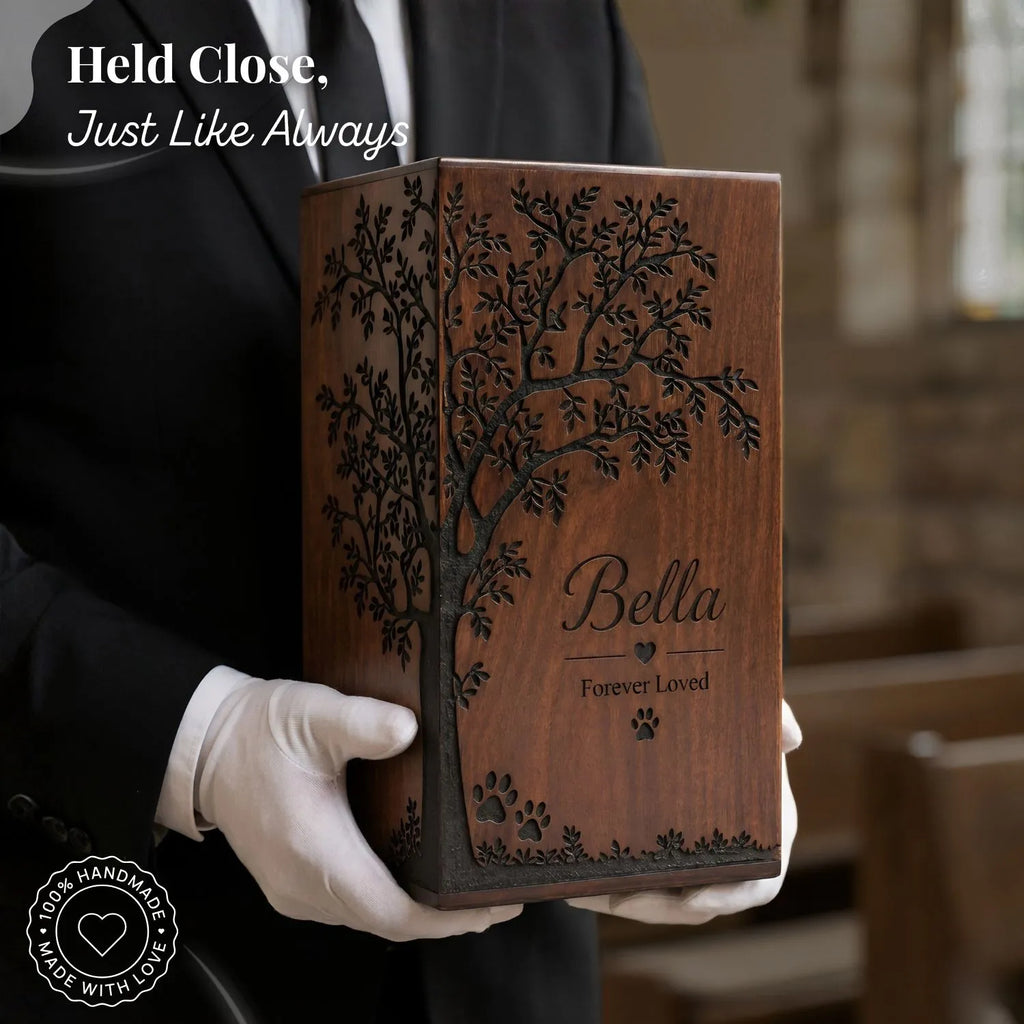 Wooden box with engraved tree and 'Bella Forever Loved' text, held by a gloved hand.