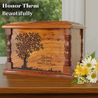 Wooden urn with engraved tree design and text, accompanied by flowers on a wooden surface.