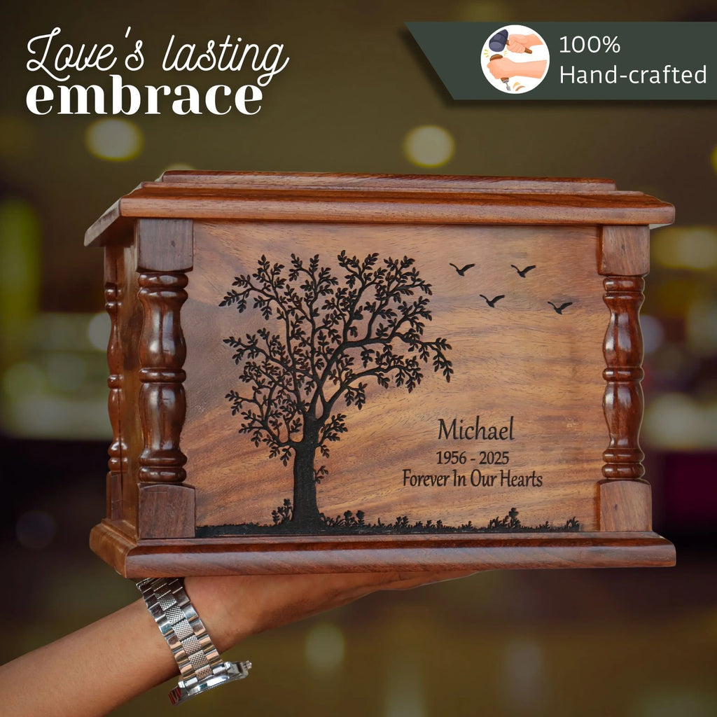 Wooden urn with engraved tree design and text, held by a hand.