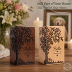 Two wooden candle holders with engraved tree design and 'Bella Forever Loved' text, placed on a surface with flowers and candles in the background.