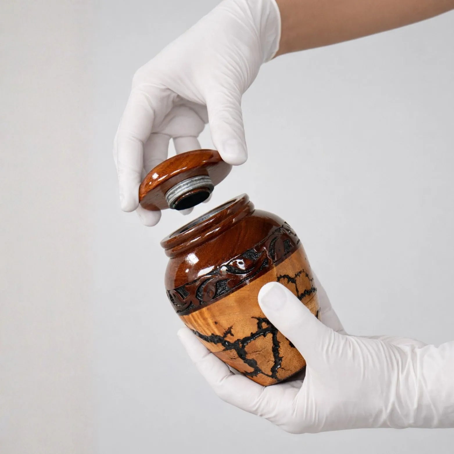 Person wearing white gloves opening a decorative jar with a white background